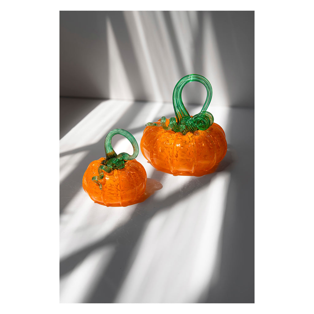 Two orange pumpkin-shaped earrings with green stems on a light background