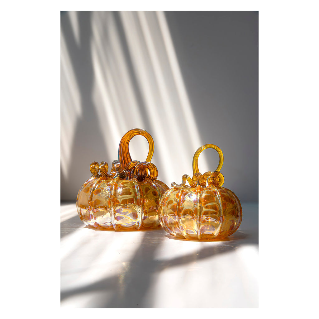 Set of three amber glass pumpkins with handles on a light surface.