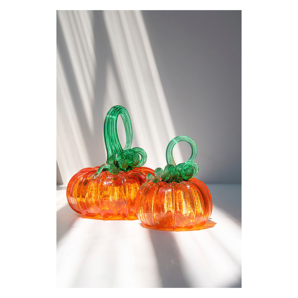 Two glass pumpkins with green stems on a white background