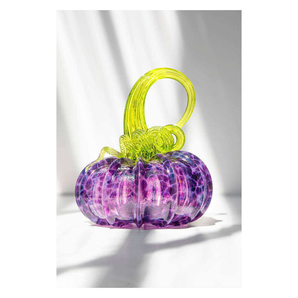 Purple glass pumpkin with a green stem on a white background