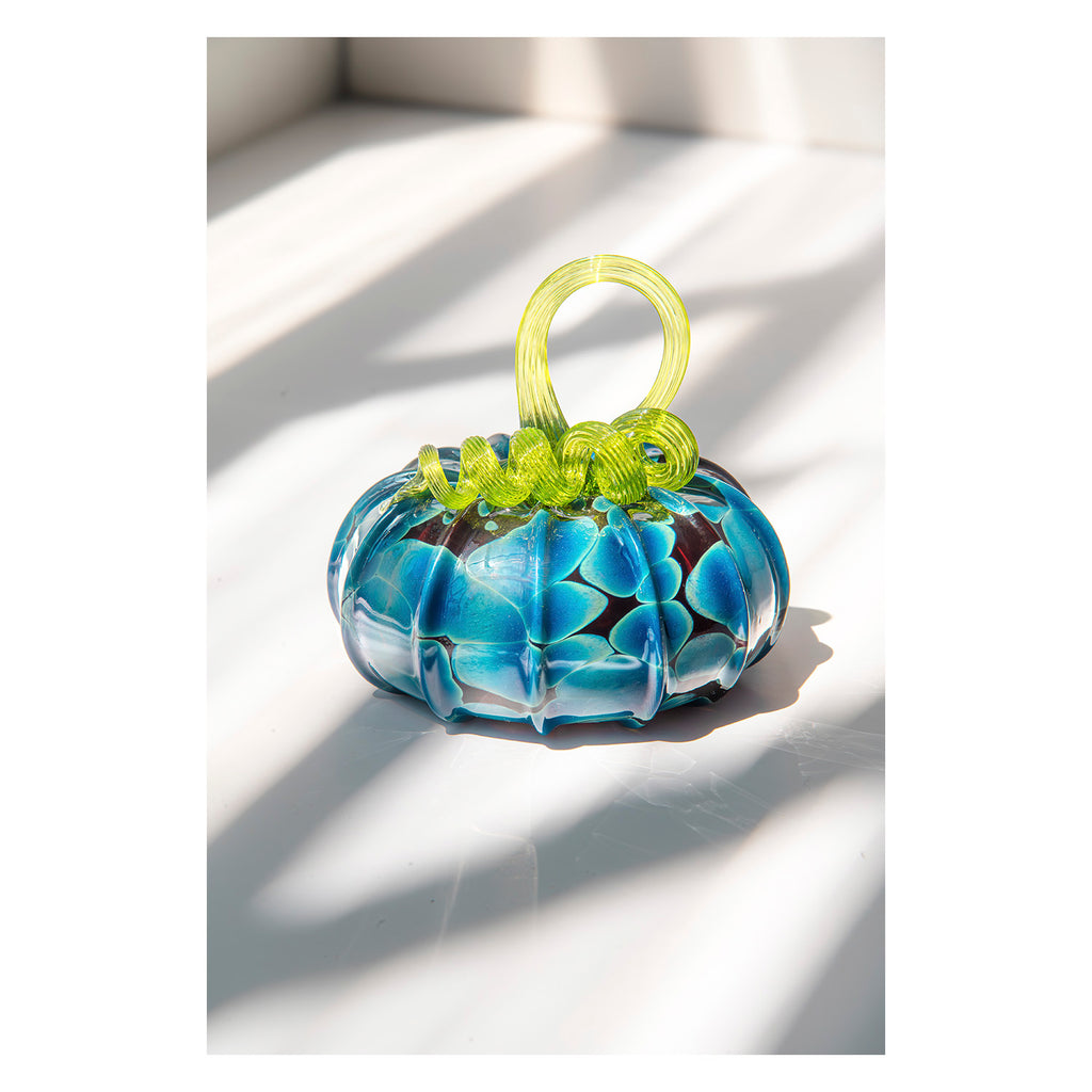 Glass pumpkin with blue and clear pattern and green stem on a white background