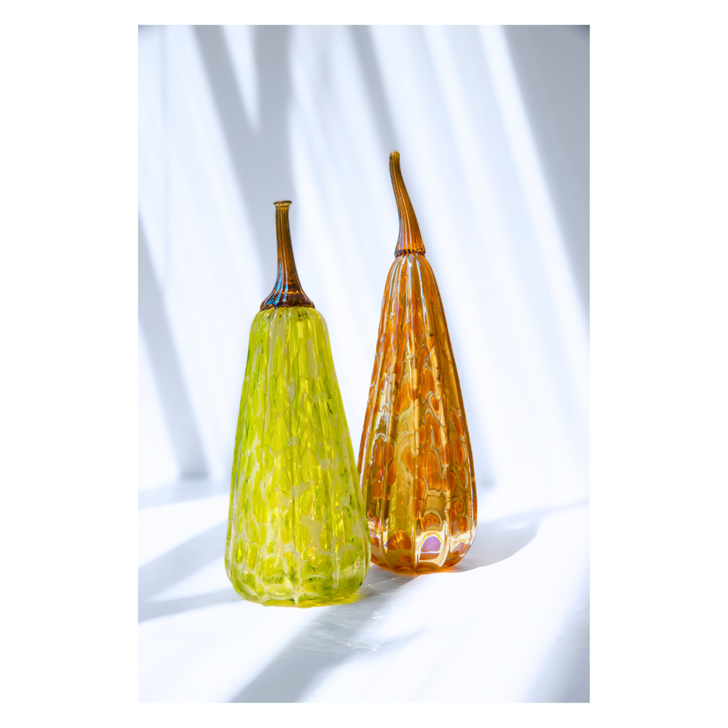 Two glass gourds, one green and one orange, on a white background