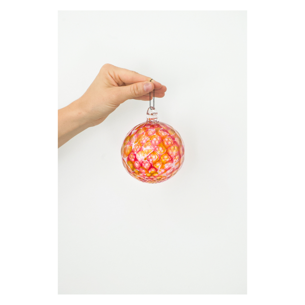 A hand holding a hand-blown glass ornament with a multicolored pattern.
