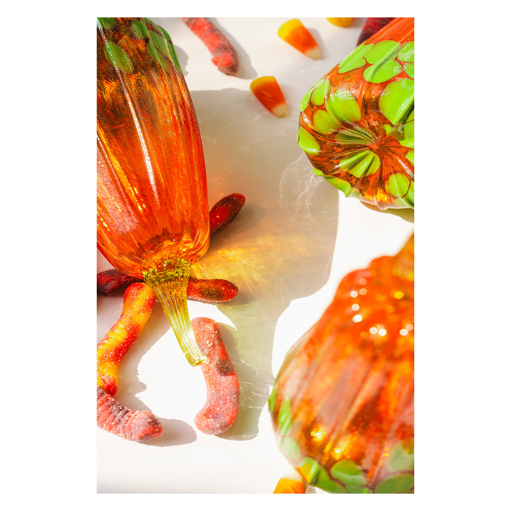 Colorful gummy worms on a white background surrounded by handblown glass pumpkin