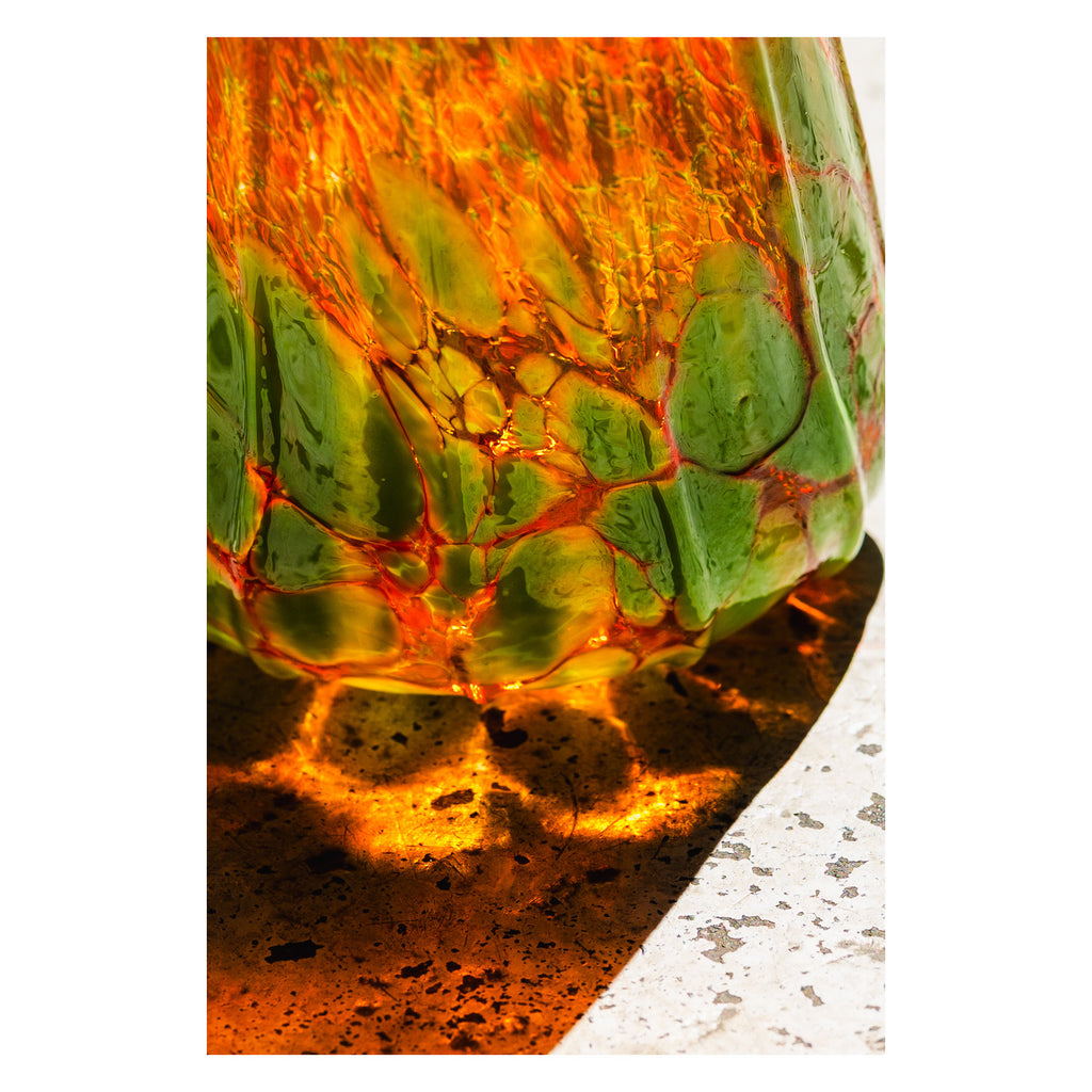 Close-up of a  handblown glass pumpkin with a green and orange marbled pattern on a white background